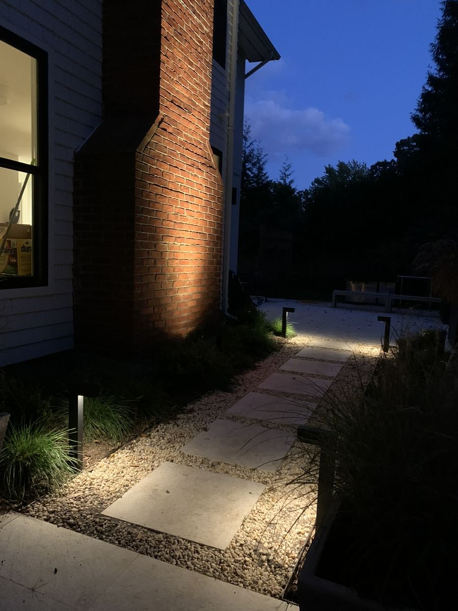 Lit walkway and uplit chimney on a Westhampton-area home at night